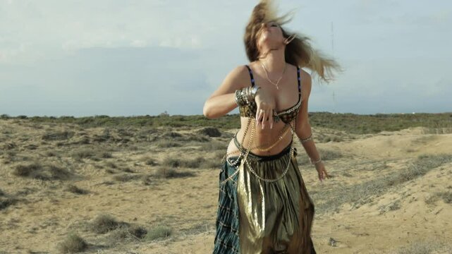 Blonde Woman in Belly Dancer Outfit Performs Gracefully in Desert, Showcasing Fluid Arm and Hand Movements Against Stunning Backdrop of Sand and Sky