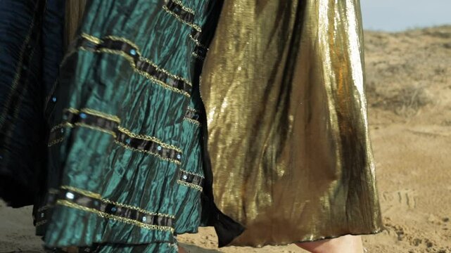 Belly Dancer Showcasing Flowing Gold and Turquoise Skirt and Adorned With Silver Bracelets Performs Gracefully on Sunlit Beach, Surrounded by Sand and Ocean Waves