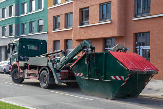 Containerdienst: LKW mit Absetzcontainer vor einem neuen Apartmentgeb&auml;ude