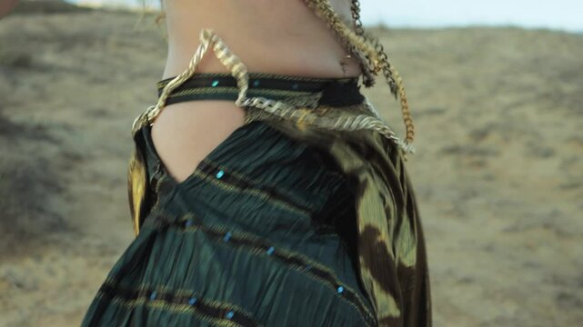 Woman with long blond hair dancing belly dance in desert. Girl wearing green and gold costume and lot of jewelry