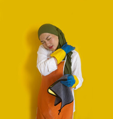 Tired Young Asian Female Housewife Massaging Her Painful Shoulder Isolated On Yellow Background. Housework And Household Concept.