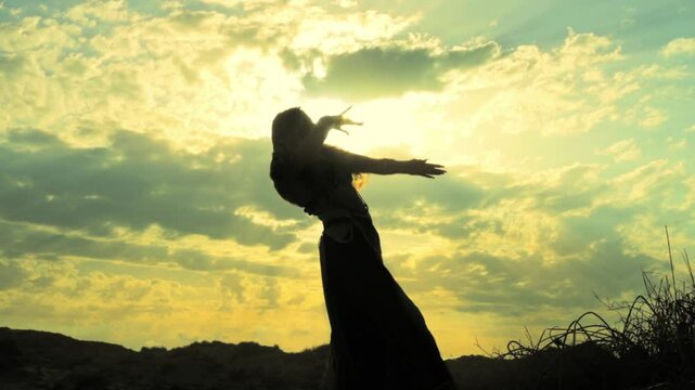 Silhouette of young woman showcasing belly dance poses against breathtaking sunset. Vibrant sky colors amplify elegance and fluidity of her movements in nature