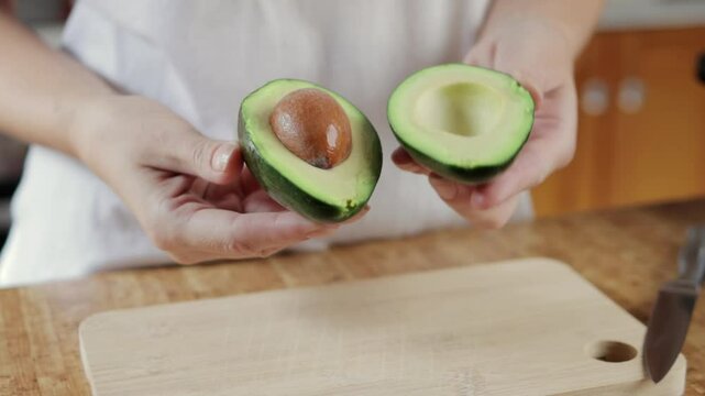 Chef cuts a fresh avocado in half and removes the seed, revealing the creamy green flesh. The avocado is ripe and ready to eat