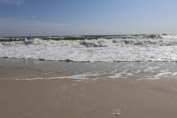 A peaceful view of ocean waves gently washing onto a sandy beach under a bright blue sky, capturing the beauty of nature and the tranquility of the seaside