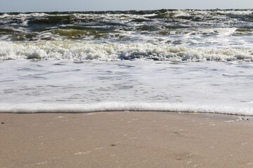 Close-up view of ocean waves creating a foamy edge as they gently reach the sandy shore under sunlight.