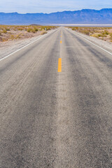 A long, empty road with yellow lines and a mountain in the background