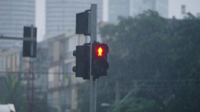 Pedestrian traffic light with red symbol for do not cross during rainy day. Heavy rain and foggy conditions in Tel Aviv in Israel. Light shows person standing still marking no crossing on cold winter
