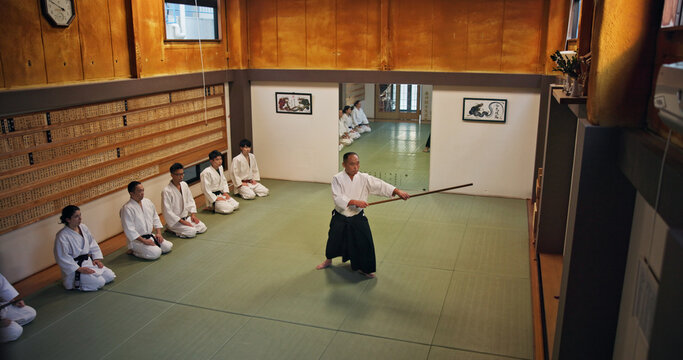 Dojo, master and demonstration of Aikido training in class with wood sword Japanese martial arts and fight exercise in studio. Learning, sport and bamboo weapon with people and strike practice above