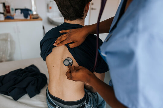 Female healthcare worker examining boy's back with stethoscope in examination room