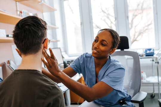 Smiling female medical professional checking lymph nodes of patient in doctor's office at hospital