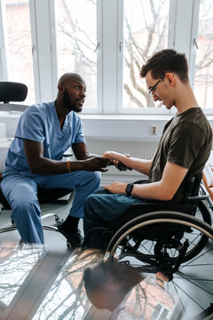 Male medical professional doing hand stretch of teenage boy sitting on wheelchair in examination room