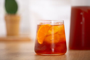 Glass of fresh cold brew coffee or cocktail with ice and slice of orange placed on wooden kitchen worktop with white background.