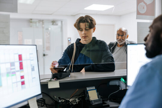 Teenage boy doing payment through smart phone at reception desk in hospital
