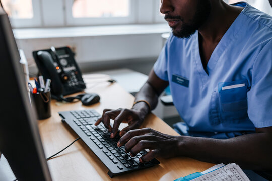 Male doctor working on computer while sitting in examination room at clinic
