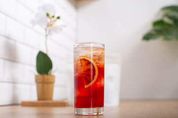 Glass of fresh cold brew coffee or cocktail with ice and slice of orange placed on wooden kitchen worktop with white background.