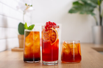 Combo of three glasses of fresh cold brew coffee, lemonade and an cocktail with ice and slice of orange and fresh mint leaves decoration, placed on wooden kitchen worktop with white background.