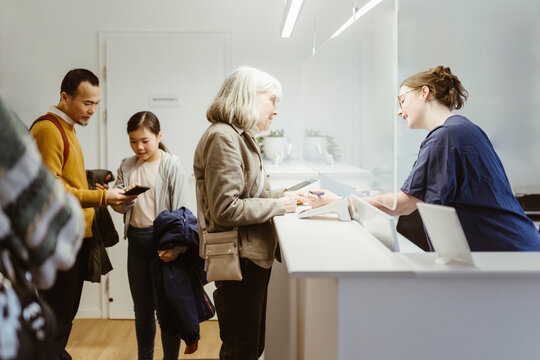 Female medical staff assisting senior woman in filling form during visit at hospital