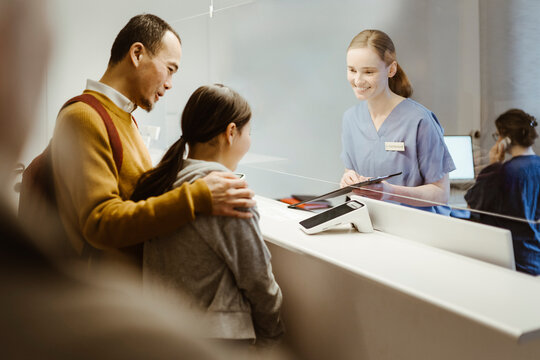 Smiling female receptionist booking appointment for girl at reception desk with father