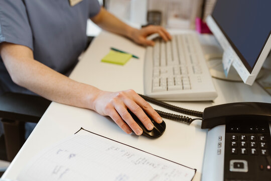 Midsection of female receptionist scrolling mouse while working at desk in hospital