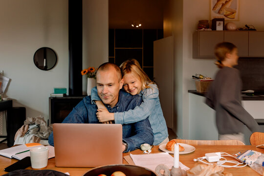Smiling boy with arm around father working on laptop at home