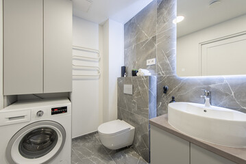 Bright Elegant Modern Luxury Home Bathroom Interior Design With White Sink. Marble Gray Walls, Mirror and Faucet. LED Mirror Lights. Heater. Shower, Tile Floor and Walls. Laundry