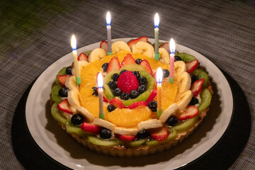 6本の火がついたろうそくが立っているフルーツタルト