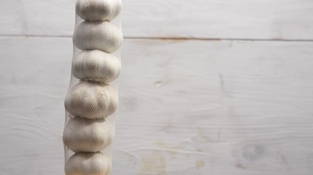 A bunch of garlic bulbs are hanging from a string. The bulbs are white and are arranged in a row. Garlic rotates on wooden background.