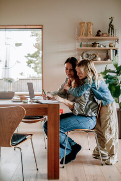 Son embracing mother working while sitting near dining table at home