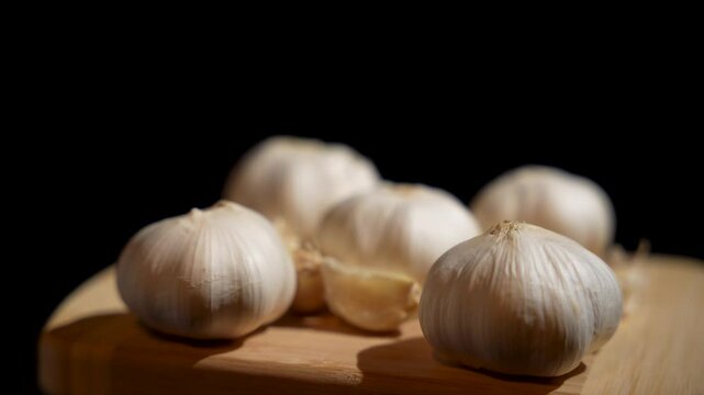A bunch of garlic cloves rotate on a wooden cutting board. The garlic is fresh and unpeeled, and the image conveys a feeling of freshness and naturalness.