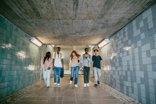 Full length of multiracial male and female teenage friends walking in underground tunnel
