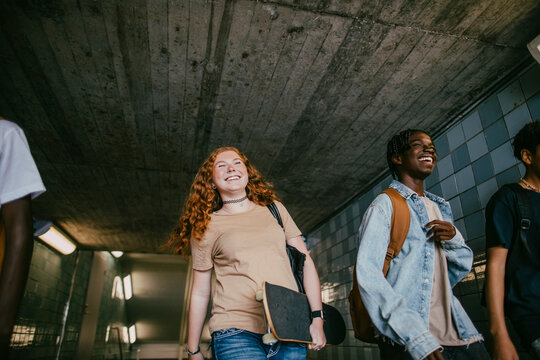 Low angle view of smiling teenage girl carrying skateboard while walking with friends in tunnel