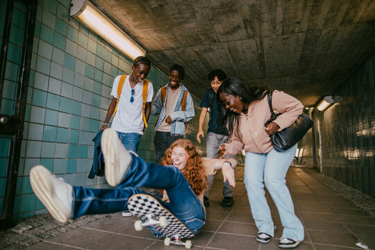 Teenage girl helping female friend losing balance on skateboard in underground tunnel