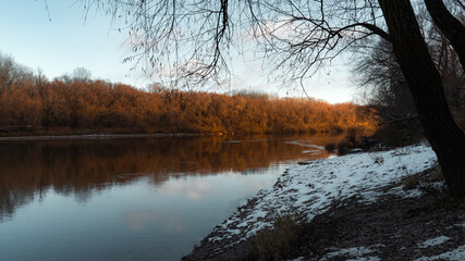 Calm river reflecting the warm golden light of sunset with snowy shores.