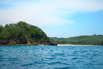 Long sea view with white cliff island with trees in the distance seen from the sea.