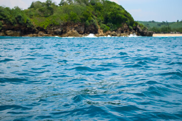 Long sea view with white cliff island with trees in the distance seen from the sea.