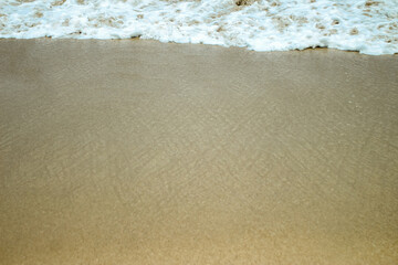 Soft waves of blue sea with foam on golden white sandy beach. Wave background