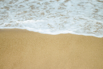 Soft waves of blue sea with foam on golden white sandy beach. Wave background