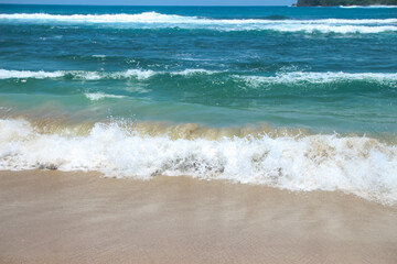 Soft waves of blue sea with foam on golden white sandy beach. Wave background