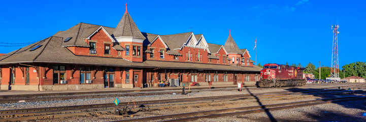 A train is pulling into a train station with a large red building in the backgro