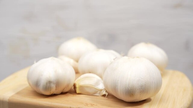 A bunch of garlic cloves are sitting on a wooden cutting board. The garlic is white and he is fresh. Concept of freshness and naturalness. Garlic rotates on wooden background.