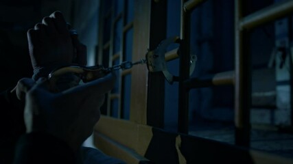 Low-key closeup of hands of unrecognizable criminal or kidnapper holding hostage in dark basement and handcuffing hands of captive to window grate, violence and torturing