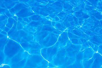 Clear blue swimming pool water surface with sunlight reflections creating abstract patterns and ripples, evoking a refreshing and tranquil summer vibe.