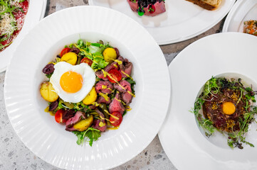 A vibrant salad featuring mixed greens, cherry tomatoes, roasted potatoes, and tender meat, topped with a perfectly poached egg. A delicious and colorful dish, ideal for healthy eating.