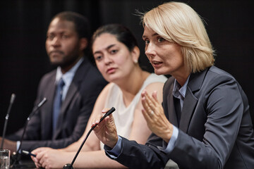 Expressive female official speaking into microphone participating in political debate during press...