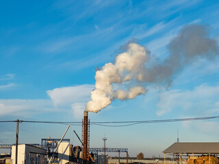 Dark smoke billows from towering smokestacks at a vast industrial facility under a clear blue sky. This setting highlights the ongoing production and pollution challenges faced by factories