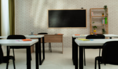 Empty modern school classroom with desks, chairs and chalkboard at daylight, workspace for learning and teaching. Full front view, blurred focus.
