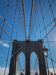 Obraz premium A sunny day walk across the iconic Brooklyn Bridge in New York City, showcasing its intricate suspension cables and stunning architectural details against a clear blue sky
