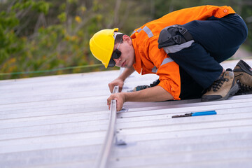 Technician on a rooftop in an orange safety uniform and helmet using tools to install a metal frame. Depicts precision, safety, and expertise in rooftop construction and renewable energy projects.