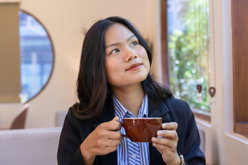 Happy businesswoman with a beautiful smile sitting at a table enjoying hot coffee or tea in the morning and a happy life, looking at something,  happiness face, drinking coffee,  business concept.