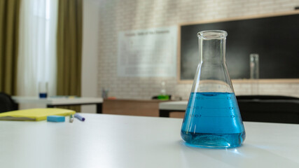 Empty school chemistry classroom with desks, chairs and chalkboard, workspace for teaching and studying. Glass bottle with blue liquid on table, close view.